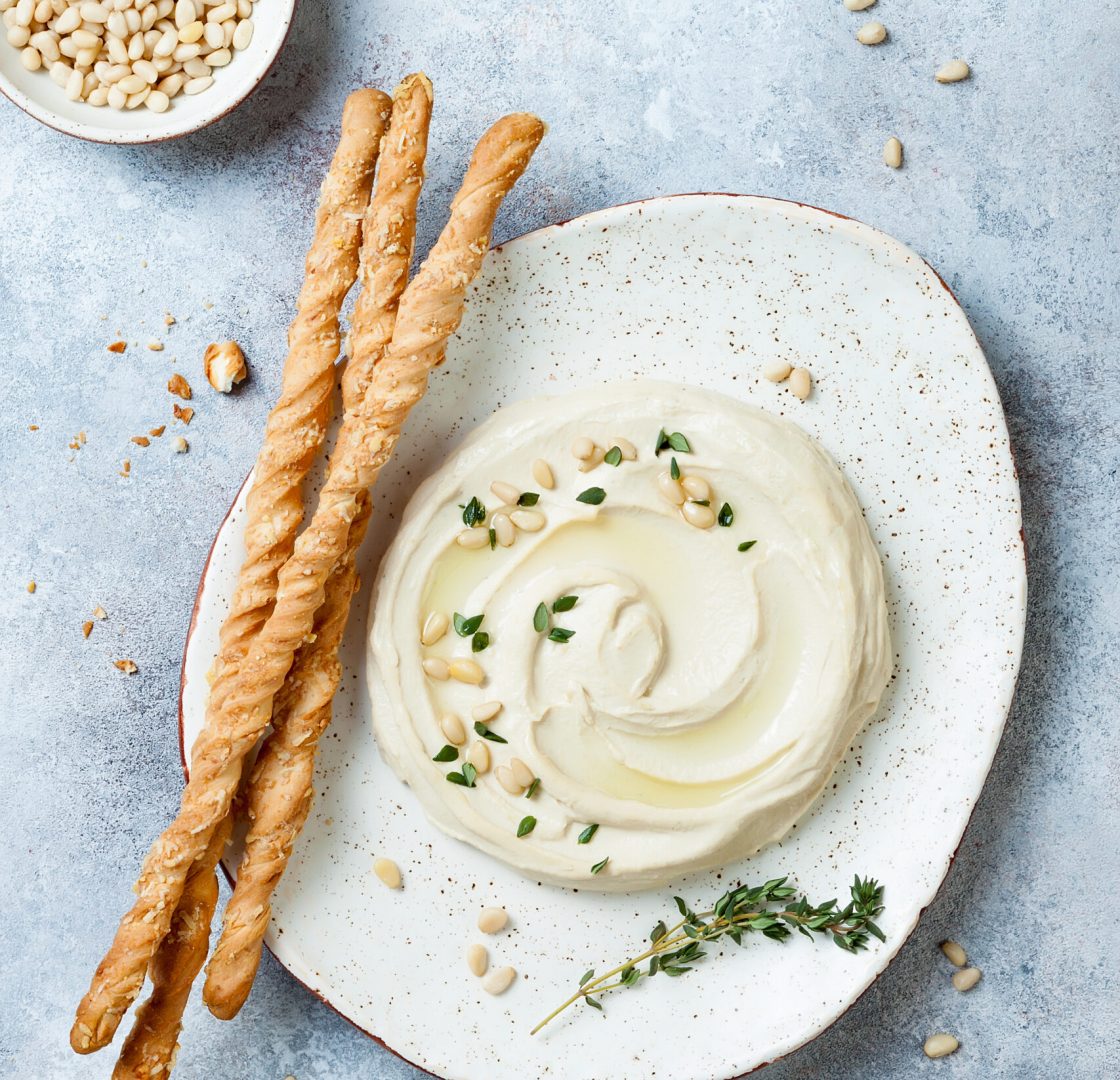 Homemade hummus with thyme, olive oil and pine nuts with grissini bread sticks. Middle Eastern traditional and authentic arab cuisine. Top view, flat lay, overhead